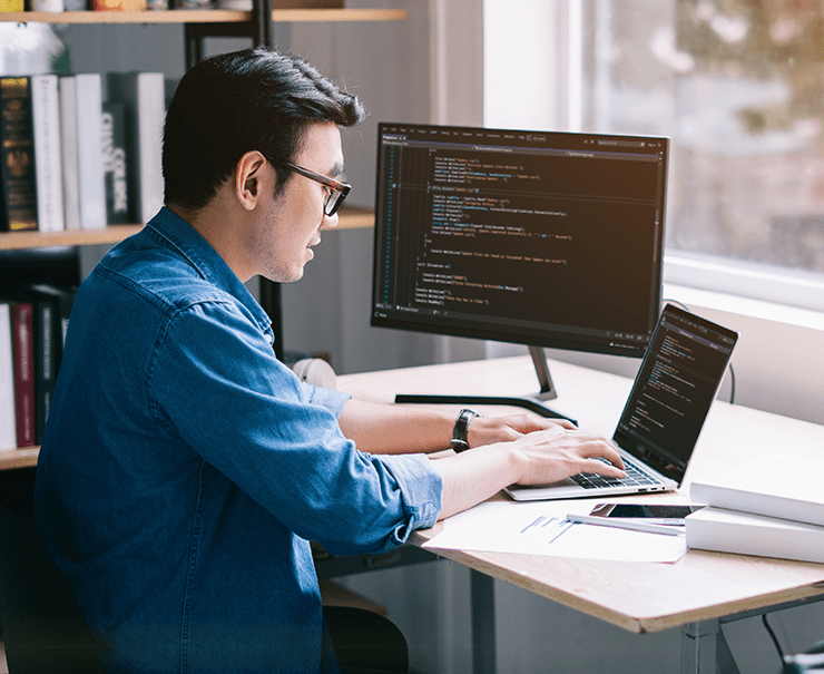 man sitting at desk software programming on two screens